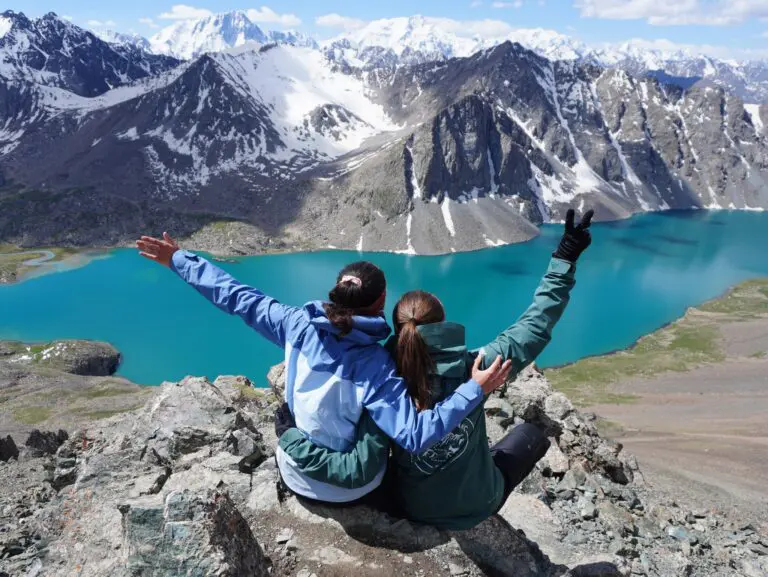 Two hikers embracing as they gaze at a turquoise mountain lake in Kyrgyzstan