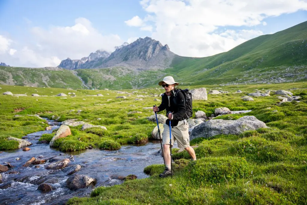 Hiker crossing a stream in a lush mountain valley