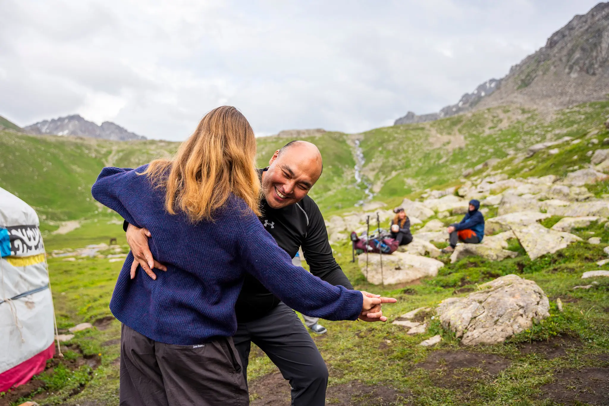 Two hikers laughing and dancing in front of a yurt in a mountain valley
