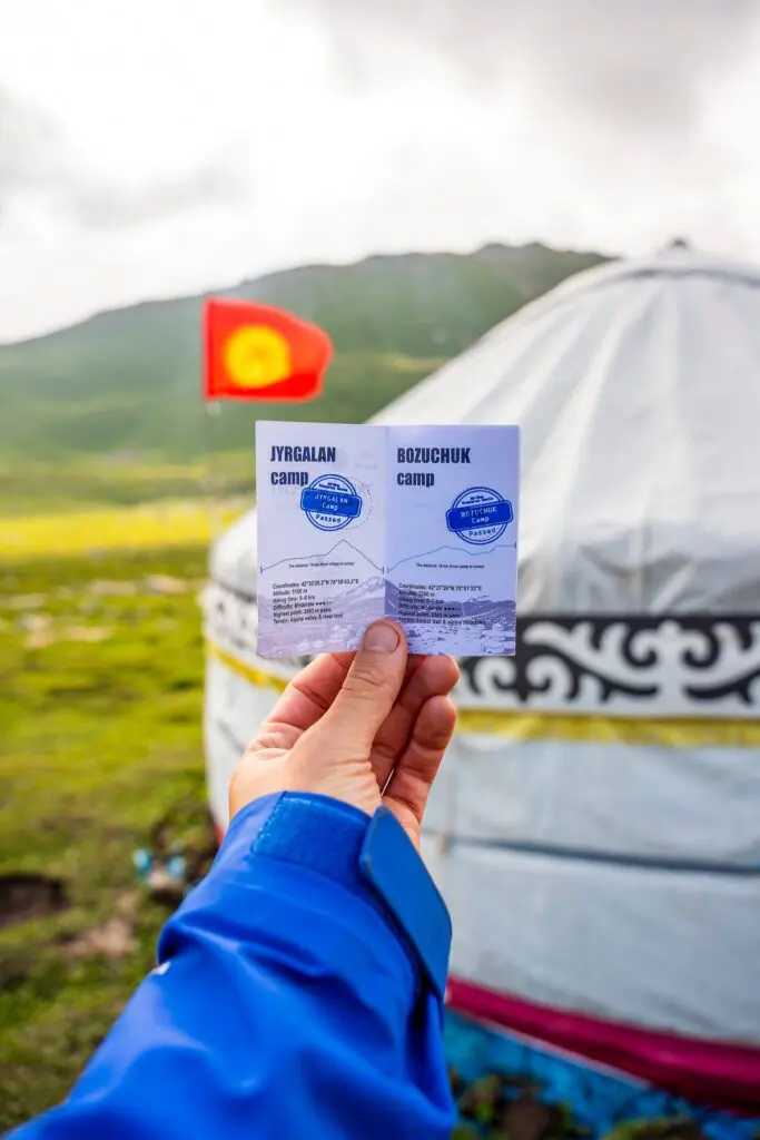 Hand holding a camp passport in front of a yurt and the flag of Kyrgyzstan