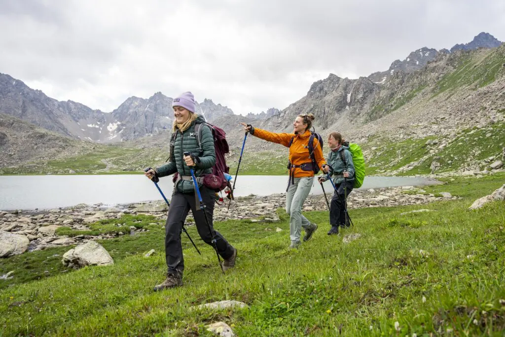 Three female hikers walking along the shore of a mountain lake in Kyrgyzstan