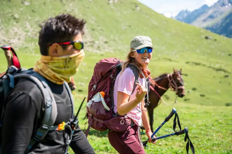 two hikers with backpacks and trekking poles in a green mountain landscape