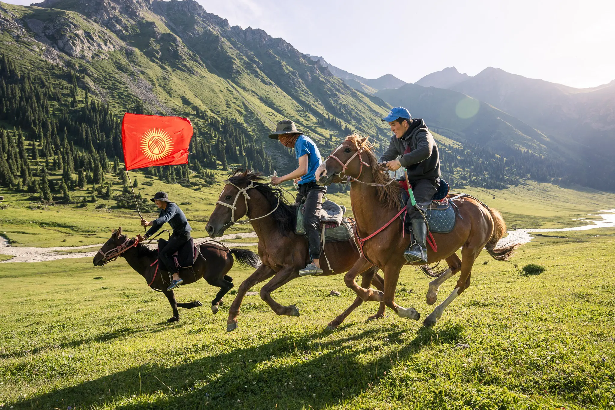 drie mannen te paard die door een groene vallei galopperen met een vlag van Kirgizië