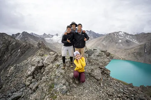 four friends posing on a rocky mountain ridge above a turquoise lake