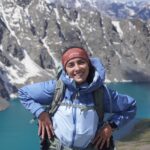 hiker smiling in front of turquoise mountain lake in Kyrgyzstan