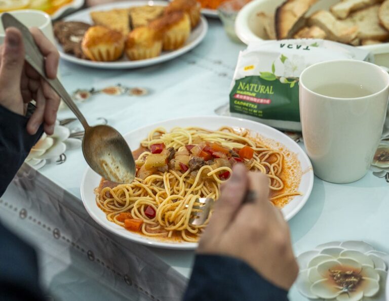 persoon die aan tafel spaghetti met groenten eet